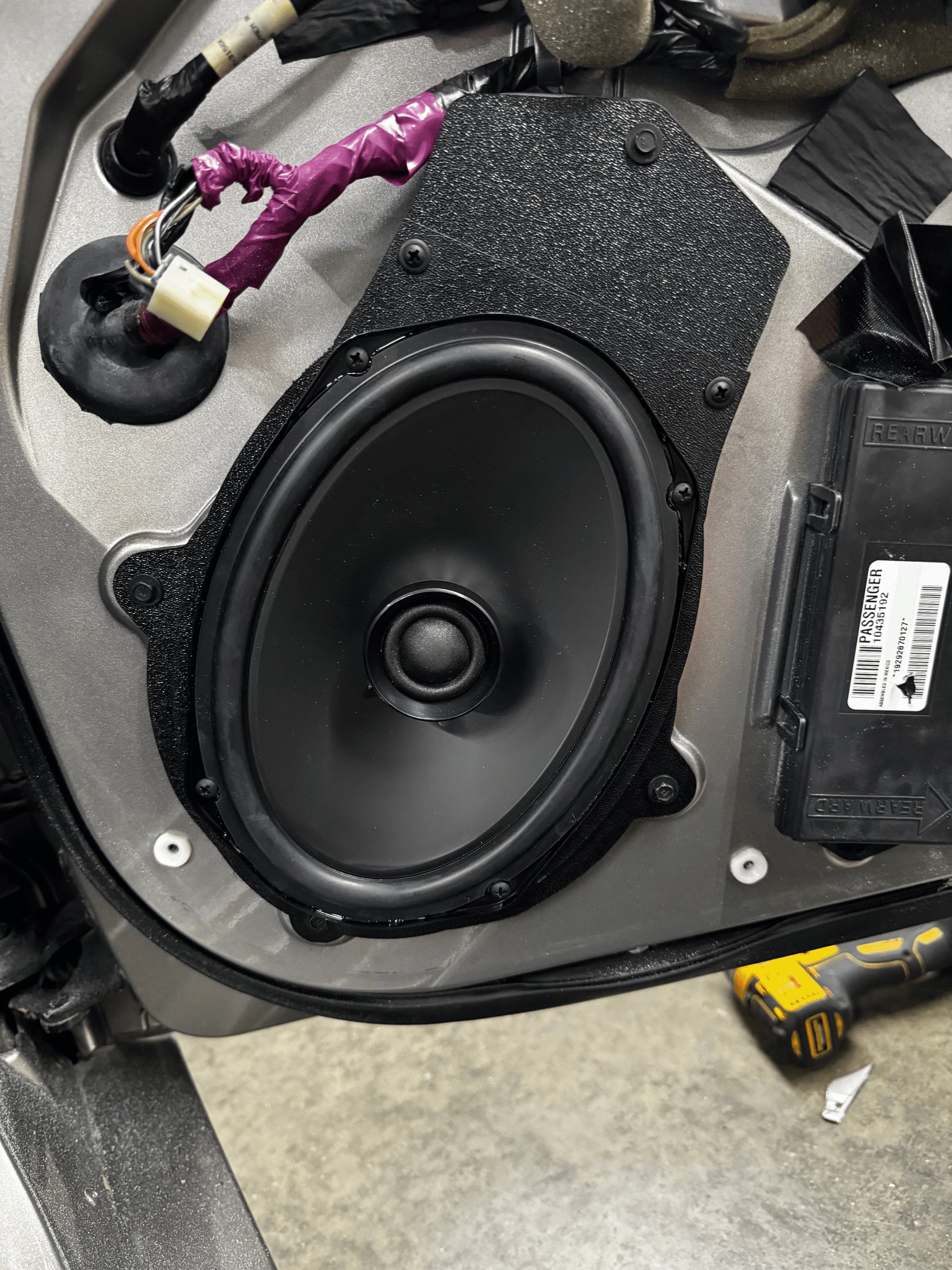 Black car speaker mounted in a vehicle door panel during installation process.